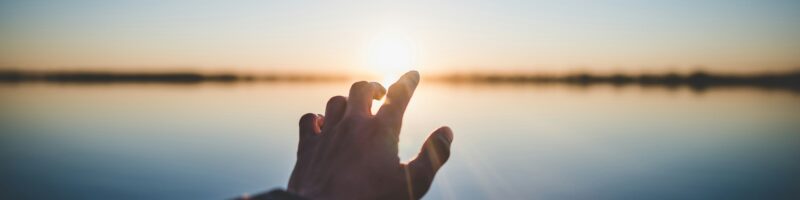 landscape photography of person's hand in front of sun