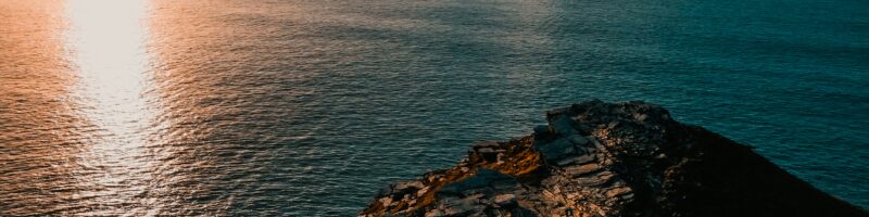 the sun is setting over the ocean with a rock outcropping
