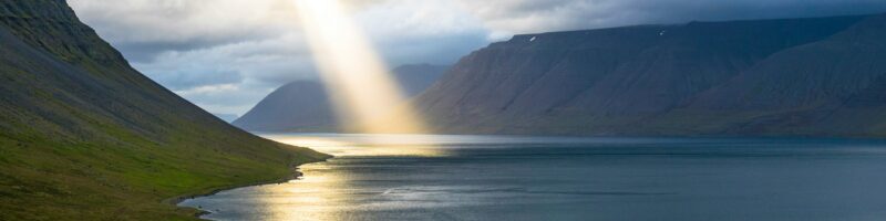 sun reflection on calm water near green mountains